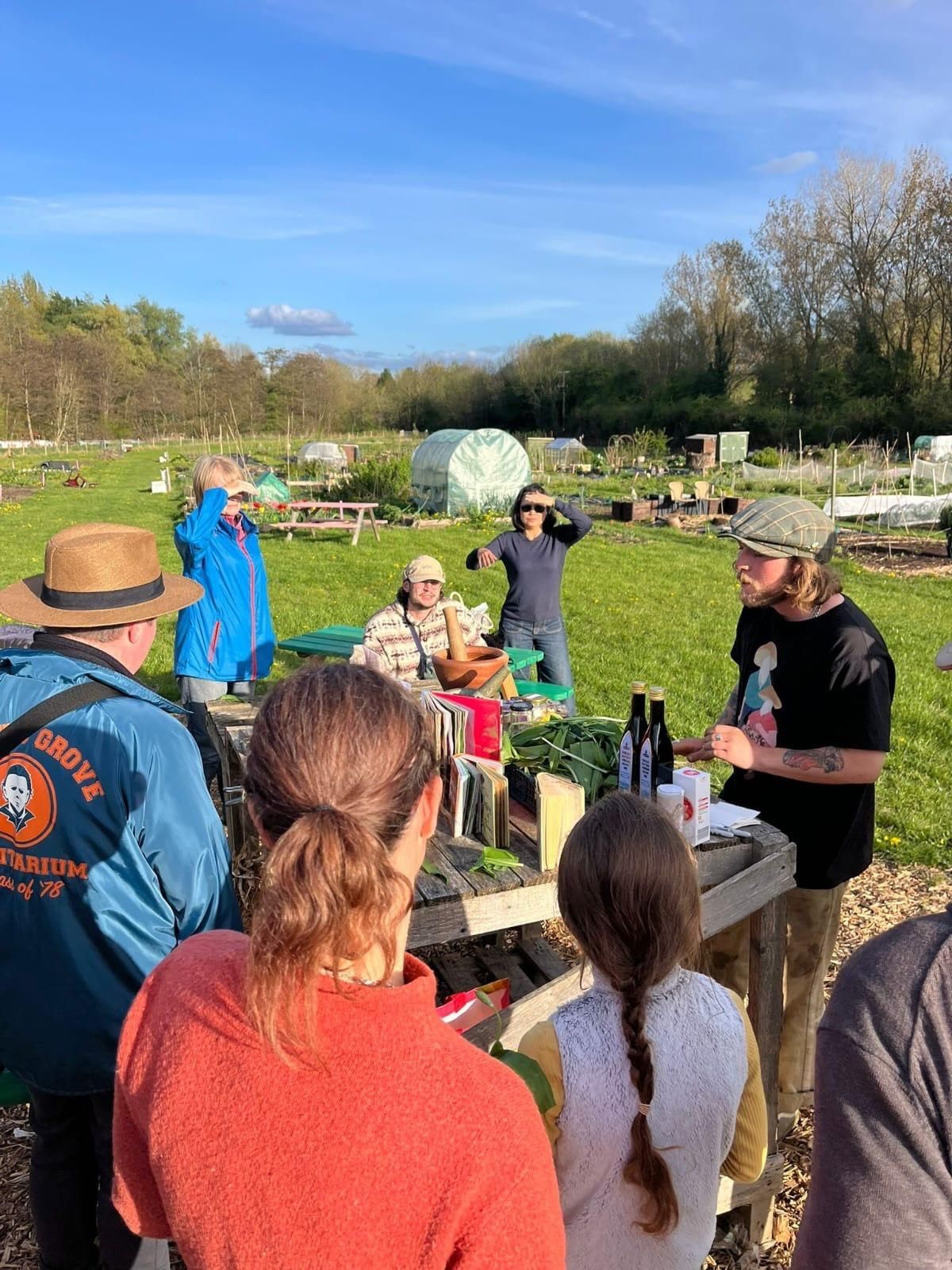 A group gathered round a trestle table spread with wild garlic, bottles and a pestle and mortar, listening to Willem.